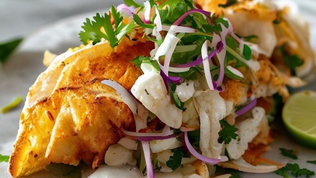 Crispy fried Baja fish taco with vibrant slaw, creamy Baja crema, and pickled red onions on a warm tortilla, proving the perfected recipe's visual appeal and texture.