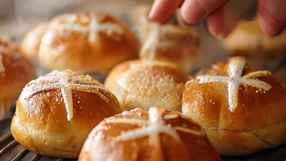 Image shows a close-up of freshly baked hot cross buns with delicate white icing crosses cooling on a wire rack, proving the successful execution of the recipe results in perfectly golden, well-formed buns ready for enjoyment.