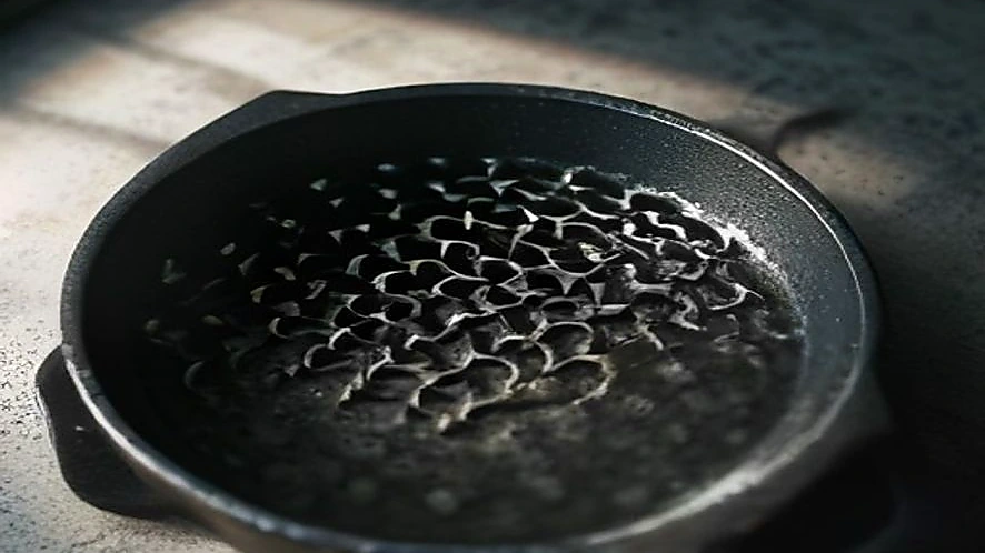 A hand scrubbing burnt residue from a cast iron pan with a stainless steel chainmail scrubber